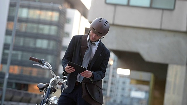 一名男子用平板电脑和智能手表在城市街道上骑自行车视频素材