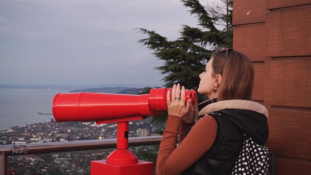 旅游:年轻的女游客在日落时用投币望远镜看城市。中景，手持，慢镜头60帧/秒视频下载