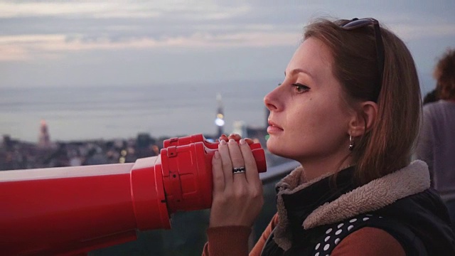 旅游:年轻的女游客在日落时用投币望远镜看城市。特写，手持，慢动作60帧/秒视频下载