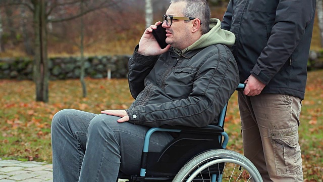 残疾人坐在轮椅上用智能手机说话，助手在后面视频素材