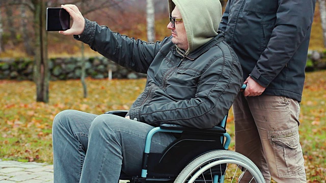 残疾人在轮椅上用智能手机拍摄，助手在后面视频素材