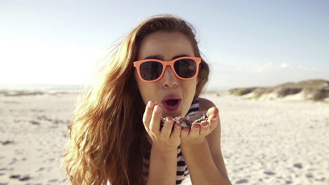 年轻女子在海滩上吹五彩纸屑视频素材
