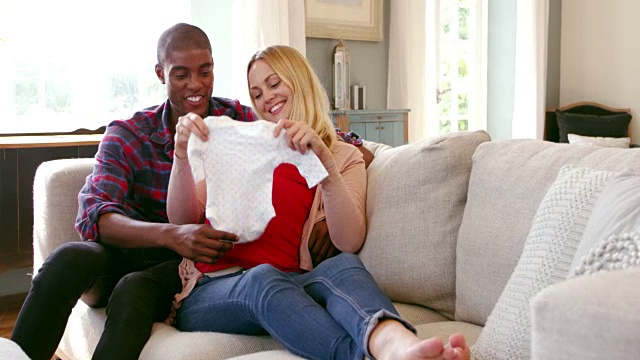 一对怀孕夫妇在家与婴儿衣服拍摄的R3D视频素材