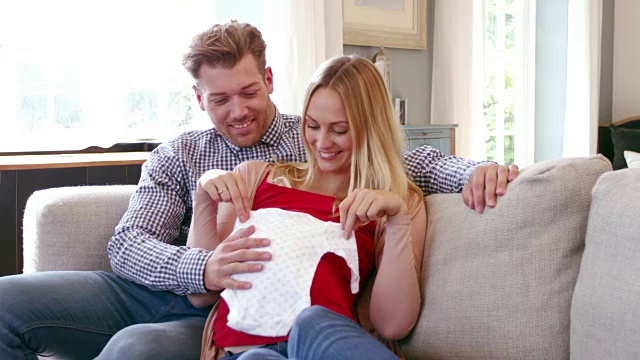 一对怀孕夫妇在家与婴儿衣服拍摄的R3D视频素材