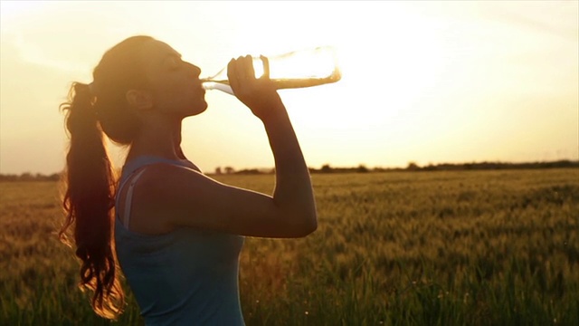 疲惫的女性慢跑者喝水美丽的夏天日落视频下载