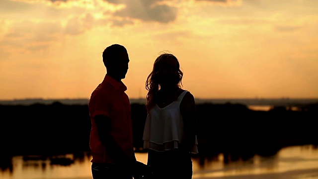夕阳下的爱情剪影。女孩展示了距离。视频素材