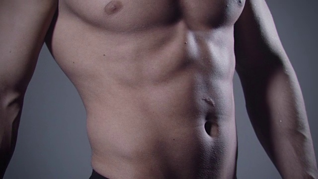 灰色背景上肌肉发达的男性身体的特写。视频下载