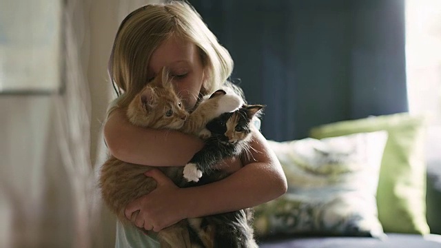 一个小女孩把两只小猫搂在怀里，亲吻它们的头视频素材