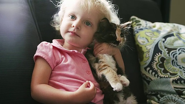 一个小女孩坐在沙发上，抱着一只小猫，给它一个拥抱视频素材