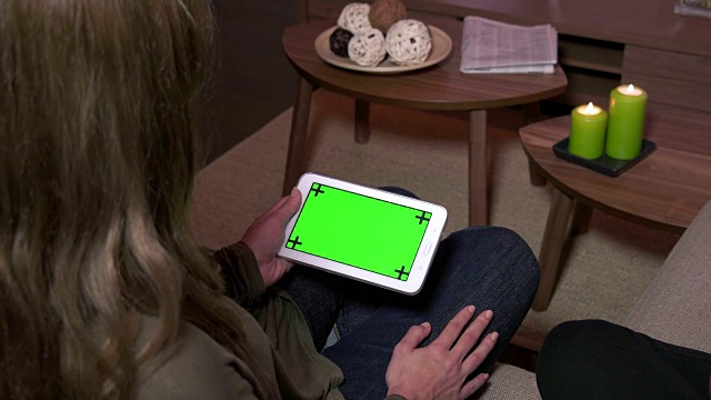 女人在沙发上触摸ipad绿色屏幕，女孩在沙发上放松，人们在使用数字平板电脑，妻子在家里看着电脑显示器。电子无线技术用于上网、发电子邮件、休闲视频素材