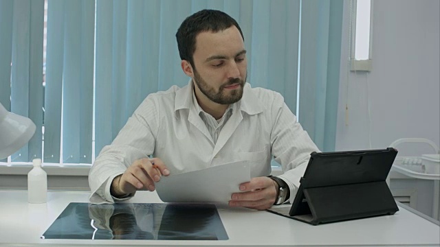 严肃的年轻大胡子医生正在用他的数码平板电脑视频下载