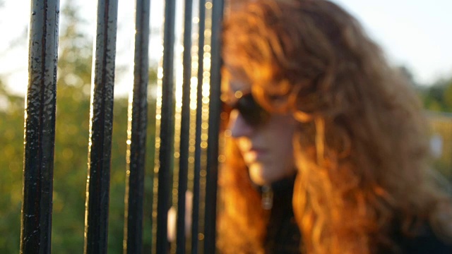 悲伤的女人在夕阳下从栏杆后面看向别处视频素材