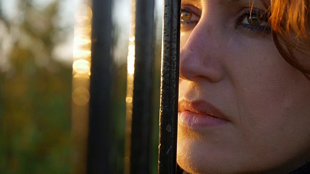 年轻的悲伤和沮丧的女人看着栏杆后面的特写镜头视频素材