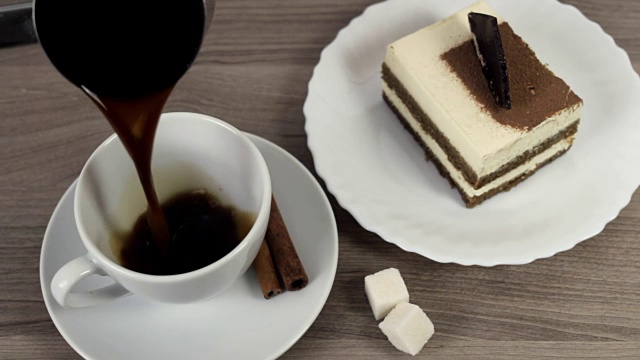 咖啡倒进木桌上的一只白色杯子里，上面放着蛋糕和肉桂视频素材