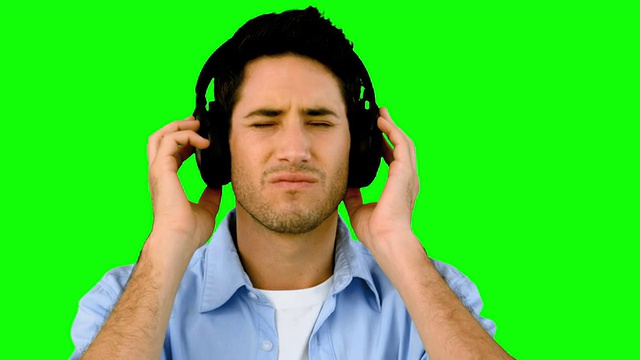 在绿色屏幕上戴着耳机听音乐的男人视频素材