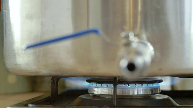 不锈钢龙头水壶和转移焦点到燃烧蓝色煤气的厨房炉子上视频素材