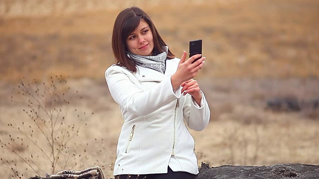 一名女子坐在枯树上玩智能手机视频下载
