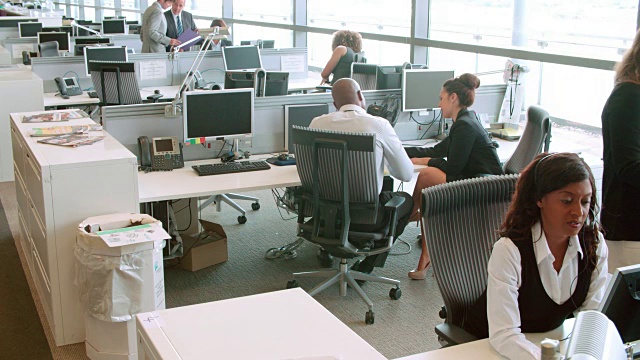 在繁忙的开放式办公室里，同事们在办公桌前聊天视频素材