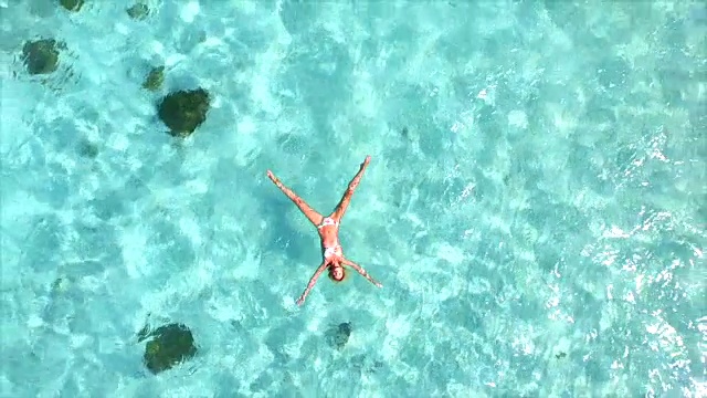 空中慢镜头:美丽的年轻女子游泳，躺在清澈的海面上视频素材