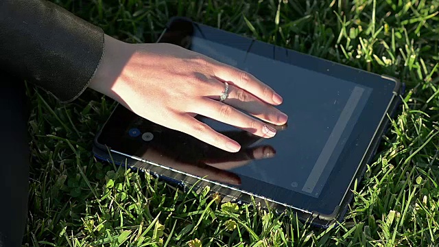 一个女孩在草地上使用平板电脑的特写视频下载