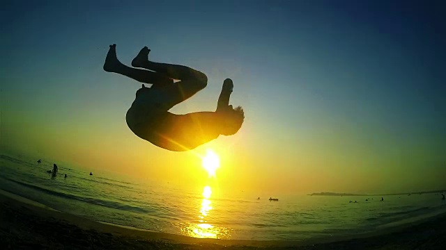 跑酷自由跑者练习后空翻在夏天的海滩日落。斯坦尼康慢动作镜头视频素材