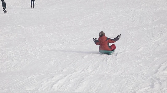小男孩从山上的雪橇上爬下来视频素材