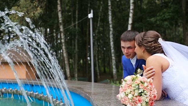 幸福的新娘和新郎站在公园的喷泉旁边视频素材