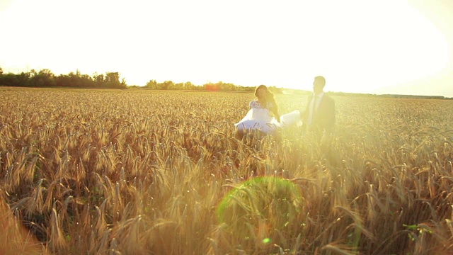 年轻美丽的一对新娘和新郎手牵着手在夕阳下奔跑在麦田里，浪漫而温柔视频下载