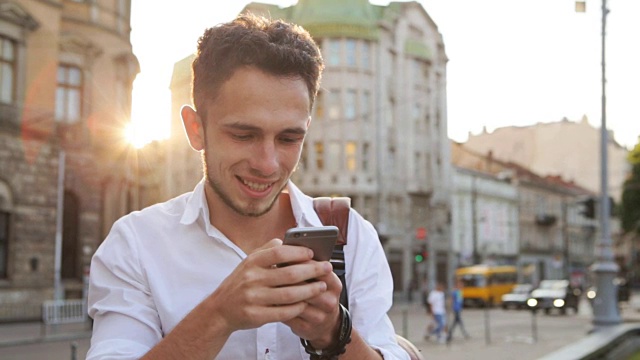 在夕阳西下的城市中心，20多岁的帅哥在智能手机上输入信息。视频下载