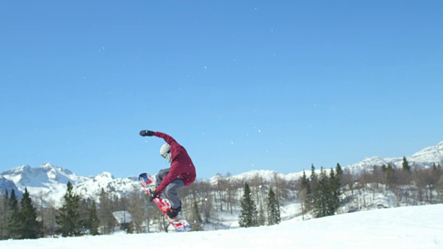慢动作:在阳光明媚的冬天，滑雪板跳跃大空中踢过摄像机在山上视频素材