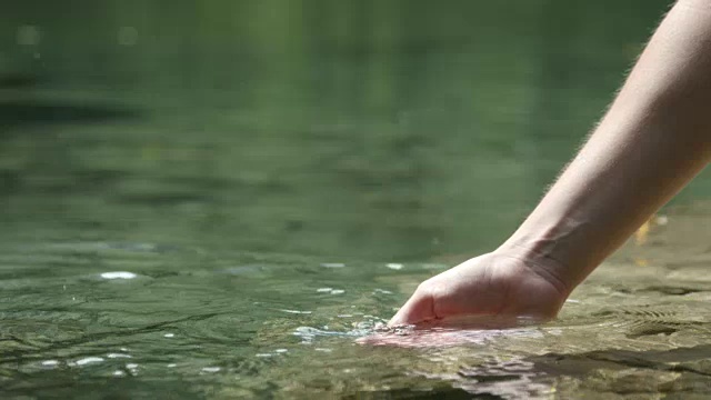 慢镜头近景:用手在美丽的山湖中玩清澈的水视频素材