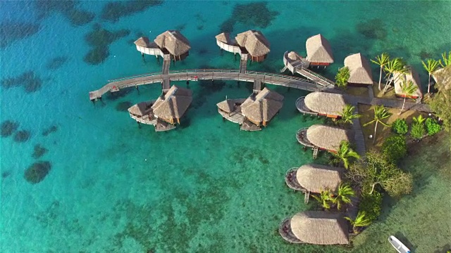 空中:大型豪华水上别墅坐落在绿松石蓝色的泻湖，郁郁葱葱的热带景观和在一个美丽的阳光明媚的热带岛屿上的豪华酒店度假村的白色沙滩。完美的浪漫的旅行视频素材