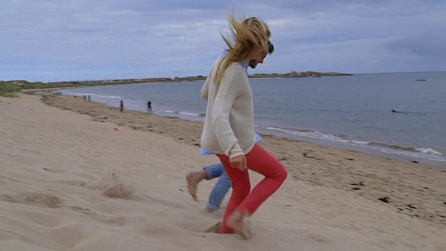 在慢镜头中，一对夫妇手牵着手沿着沙丘奔向大海视频下载