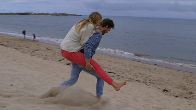 一名男子背着一名女子，沿着沙丘向大海缓慢奔跑视频下载