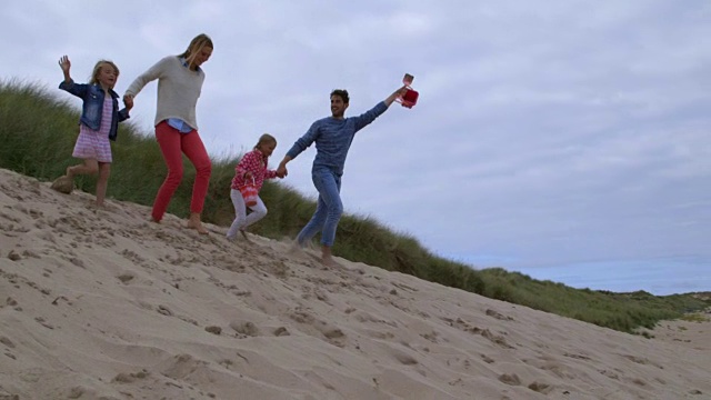 一家人在海滩度假时一起跑过沙丘的慢镜头视频素材