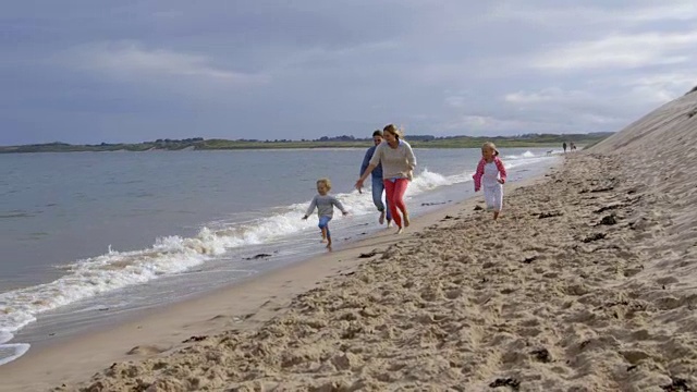 在慢镜头中，父母们沿着海岸线追逐着孩子们视频素材