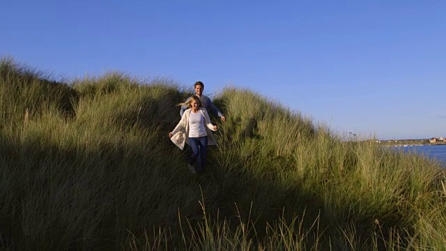 一对夫妇一起跑过沙丘的慢镜头视频下载
