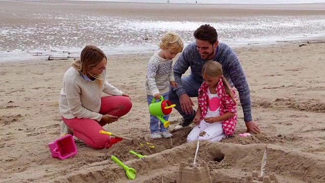 一个家庭，孩子们在海滩上建造沙堡-男孩从玩具喷壶倒水视频素材