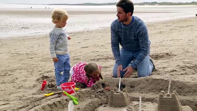 父亲和孩子们一起在海滩上建造沙堡视频下载