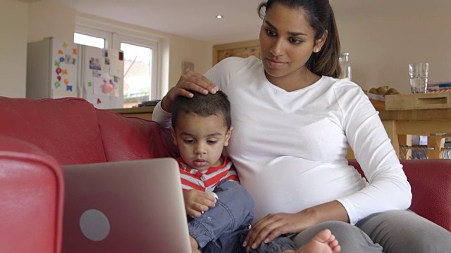 怀孕的母亲和儿子在沙发上看笔记本电脑视频素材