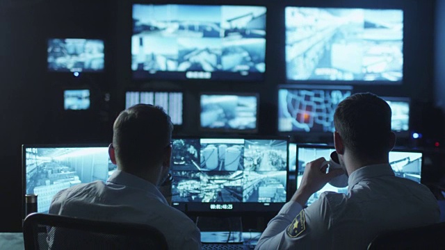 两名安全人员正在一间充满电脑显示屏的黑暗监控室中工作。视频素材