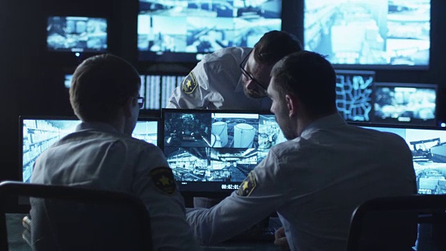 一群安全人员正在一间充满显示屏的黑暗监控室里进行工作对话。视频素材