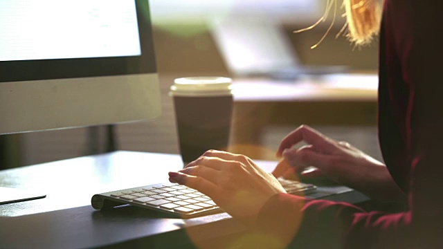 一个年轻女子在一张桌子前用电脑键盘工作。太阳光的光学耀斑。视频下载