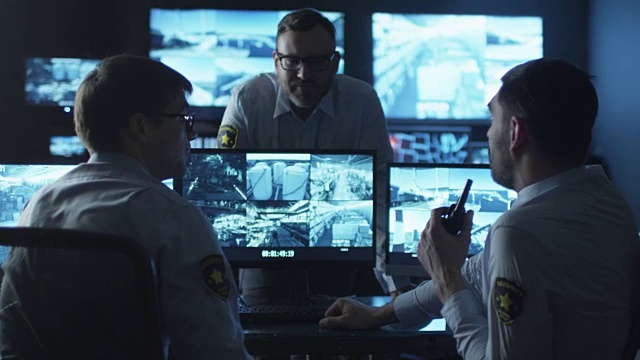 一群安全人员正在一间充满显示屏的黑暗监控室里进行工作对话。视频素材