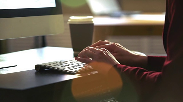 一个年轻女子在一张桌子前用电脑键盘工作。太阳光的光学耀斑。缓慢的运动。视频素材