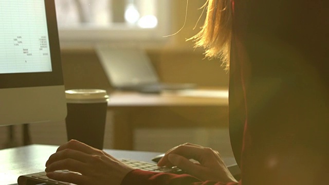 一个年轻女子在一张桌子前用电脑键盘工作。太阳光的光学耀斑。视频素材