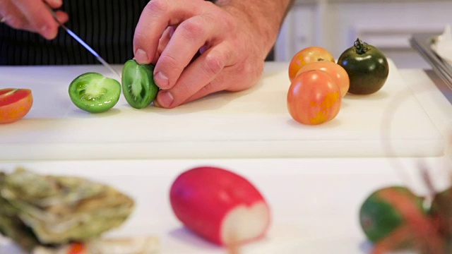 厨师把绿番茄切成两半，摄像机移到右边，特写视频下载