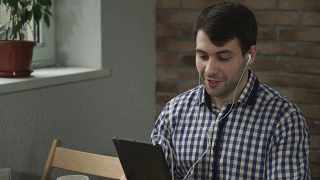 一名手持平板电脑的男子戴着耳机，欢迎同伴在线视频下载