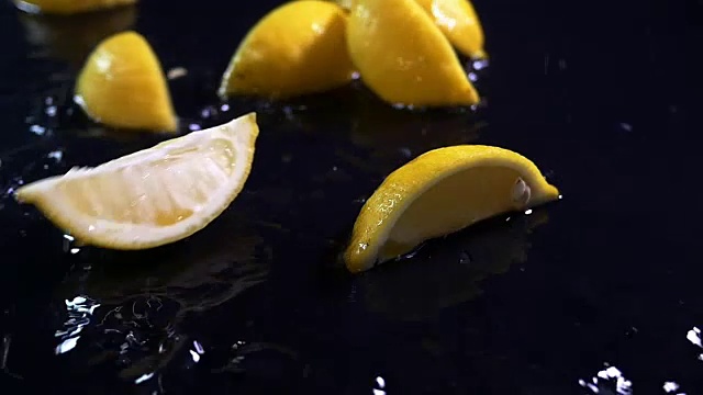 慢动作柠檬随着水滴落在黑色的表面上。视频下载