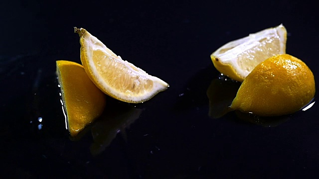慢动作柠檬随着水滴落在黑色的表面上。视频下载